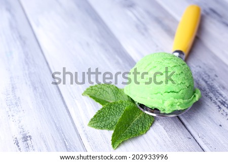 Spoon with tasty ice cream ball on color wooden background
