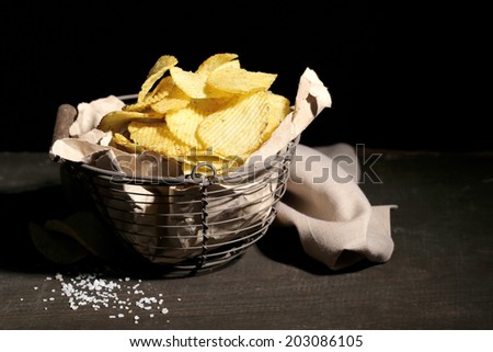 Tasty potato chips in metal basket  on wooden table with dark light