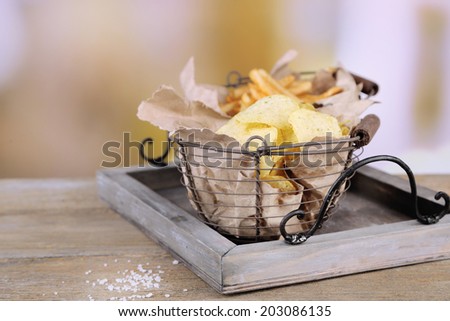 Tasty potato chips and french fries in metal baskets on wooden table, on light background