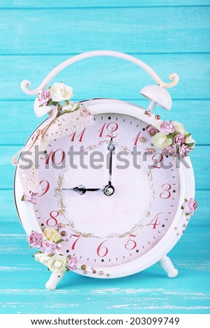 Beautiful vintage alarm clock with flowers on blue wooden background