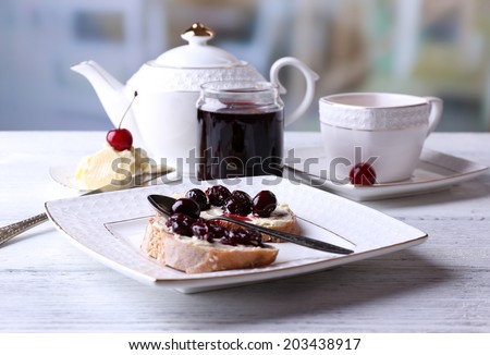 Fresh bread with cherry jam and homemade butter on plate on wooden table, on bright background