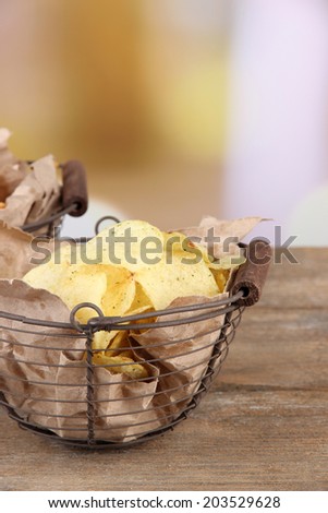 Tasty potato chips in metal basket on wooden table, on light background