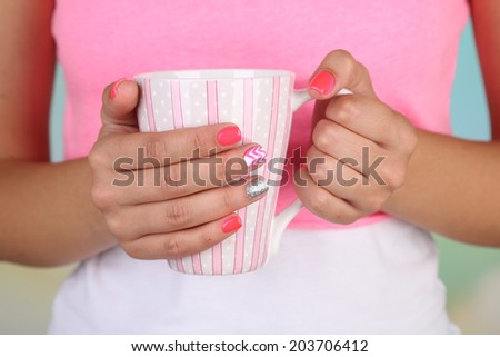 Woman with stylish colorful nails holding mug, close-up, on color background