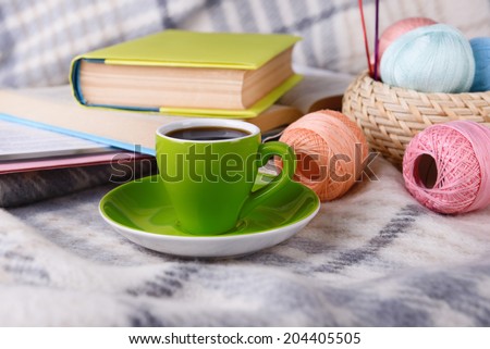 Cup of coffee and yarn for knitting on plaid with books close-up