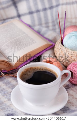 Cup of coffee and yarn for knitting on plaid with book