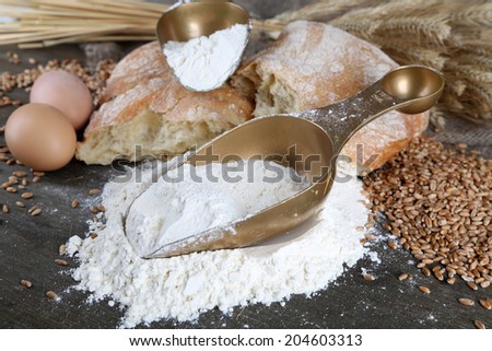The wholemeal flour in scoops on wooden table on sackcloth background