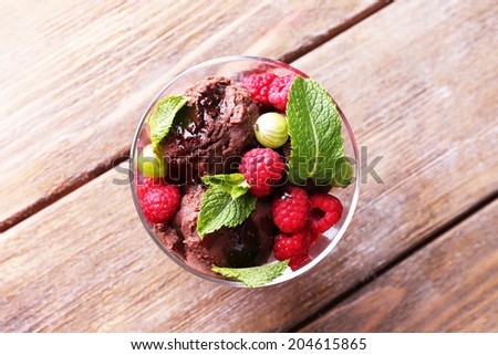 Chocolate ice cream with mint leaf and ripe berries in glass bowl, on color wooden background