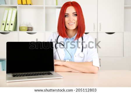 Young beautiful doctor with laptop in cabinet