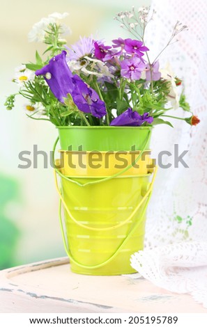 Bouquet of colorful flowers in decorative bucket, on chair, on bright background
