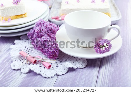 White cup with delicious dessert and lilac flowers on wooden table