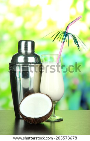 Pina colada drink in cocktail glass and metal shaker, on bright background
