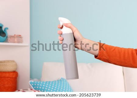 Sprayed air freshener in hand on home interior background