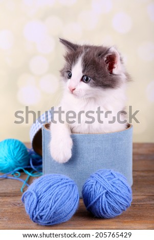 Cute little kitten in box playing with thread ball, on light background
