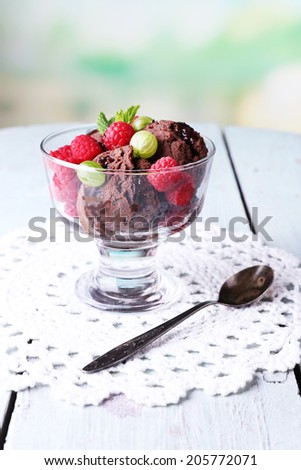 Chocolate ice cream with mint leaf and ripe berries in glass bowl, on color wooden table, on bright background