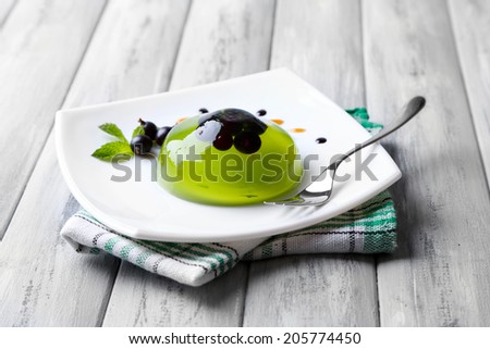 Green jelly with blackcurrant berries and sauce, on wooden background