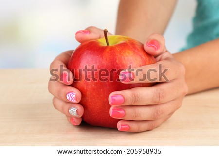 Female hand with stylish colorful nails holding red apple, close-up, on color background