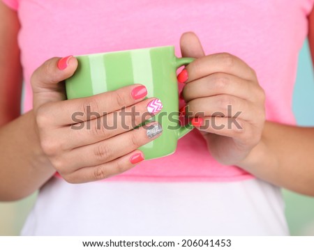 Woman with stylish colorful nails holding mug, close-up, on color background