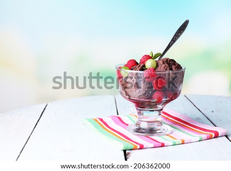 Chocolate ice cream with mint leaf and ripe berries in glass bowl, on color wooden table, on bright background