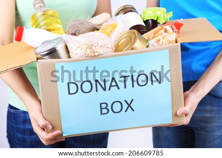 Volunteers with donation box with foodstuffs on grey background