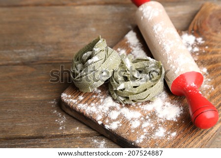 Assortment of colorful pasta in bags, rolling-pin on cutting board, on wooden background