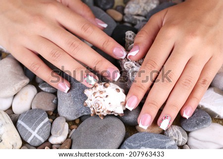 Female hand with stylish colorful nails on sea pebble background