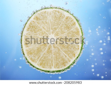 Fresh lime in water with bubbles on blue background