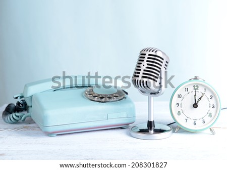 Vintage microphone,phone and alarm clock on table on light blue background