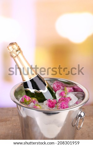 Frozen rose flowers in ice cubes and champagne bottle in bucket, on bright background