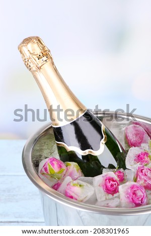 Frozen rose flowers in ice cubes and champagne bottle in bucket, on light background