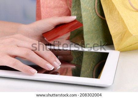 Female hands holding credit card with computer tablet and paper bags on table close up