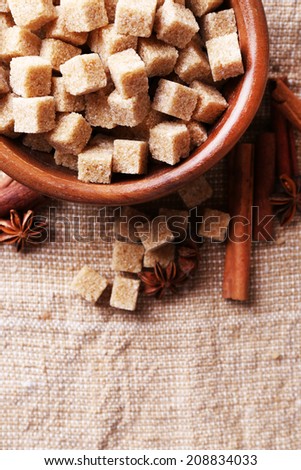 Brown sugar cubes and crystal sugar, spices in bowl on sackcloth background