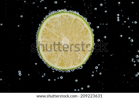 Fresh lime in water with bubbles on black background