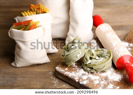 Assortment of colorful pasta in bags, rolling-pin on cutting board, on wooden background
