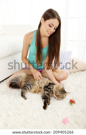 Beautiful young woman with cat sitting on carpet in room