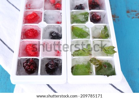 Ice cubes with forest berries, mint leaves in ice cube tray, on color wooden background