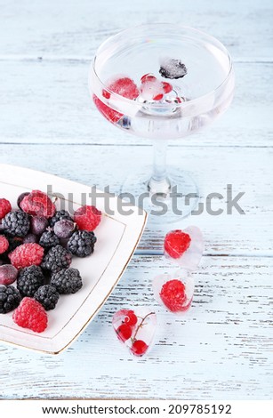 Frozen forest berries on plate and cocktail with berries, frozen in ice cubes on wooden table background
