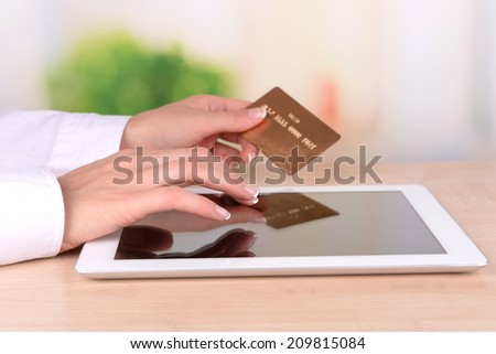Female hands holding credit card and computer tablet on table on bright background