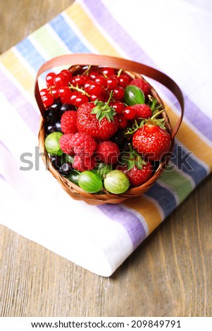 Forest berries in wicker basket, on wooden background