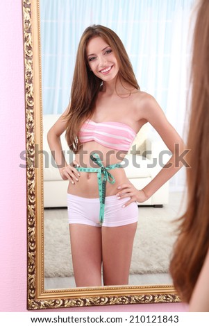 Beautiful woman with measuring tape posing near mirror in room