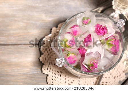Ice cubes with rose flowers in glass bucket and two glasses with champagne on wooden table background