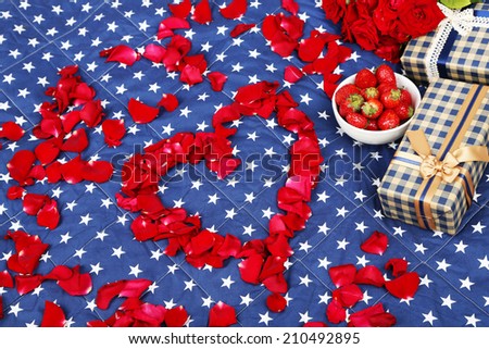 Romantic still life with strawberry, gift boxes and petals of roses on bed