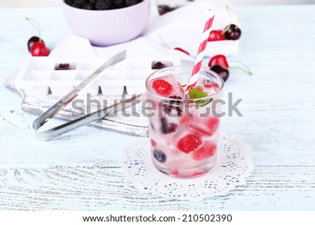 Cold cocktail with forest berries, frozen in ice cubes on wooden table background