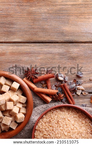 Brown sugar cubes, reed and crystal sugar in bowl with spices on wooden background