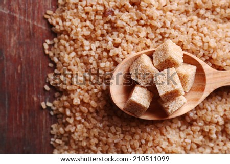 Brown sugar cubes in wooden spoon on crystal sugar background