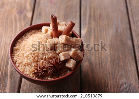 Brown sugar cubes and crystal sugar with spices in bowl on wooden background
