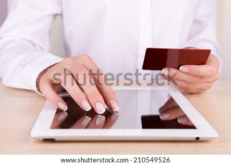 Female hands holding credit card and computer tablet on table close up