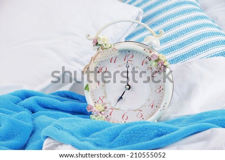 Metal clock on blue pillows on a big white bed