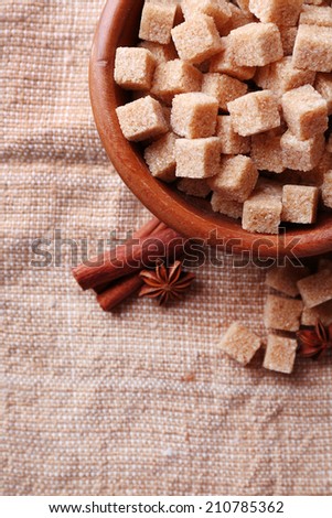 Brown sugar cubes and crystal sugar, spices in bowl on sackcloth background