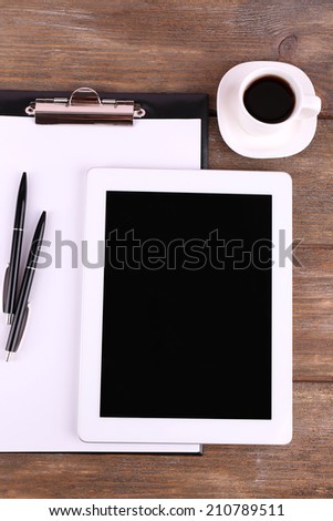 Tablet, cup of coffee, pens and folder with paper on wooden background