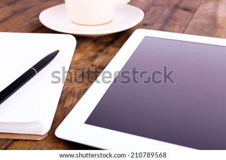 Tablet, cup of coffee, notebook and pen on wooden background